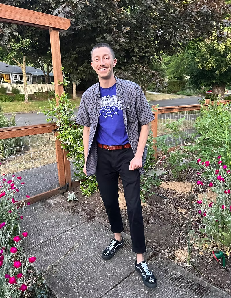Rob Schenk standing in a garden wearing a patterned shirt and black pants